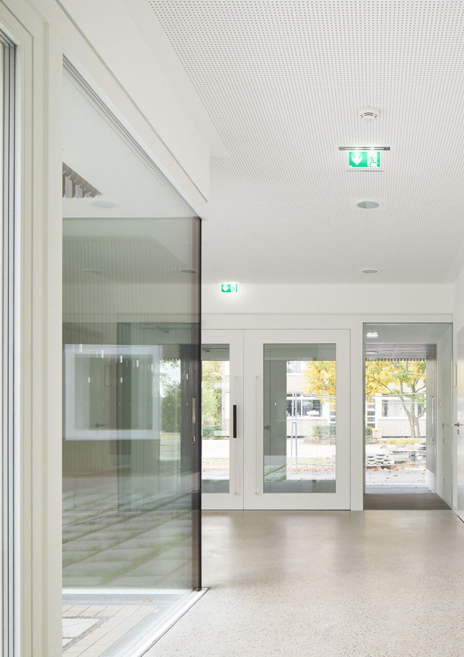 Zu sehen ist der Eingangsbereich von innen mit weißen Wänden und einem hellgrauen Boden.