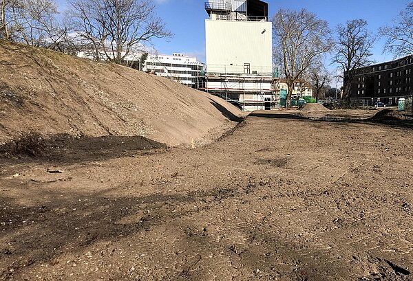 Areal mit aufgeschütteter Erde. Turm im Hintergrund