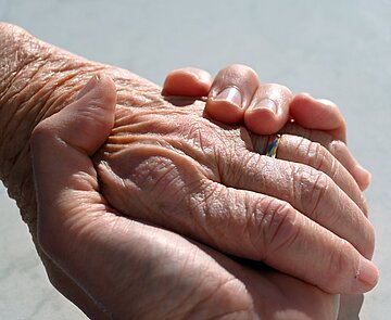 Eine Hand eines jungen Menschen hält die Hand einer älteren Person.