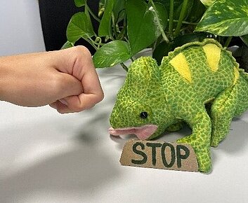 Stoffchamäleon mit Schriftzug Stopp wird von Faust bedroht