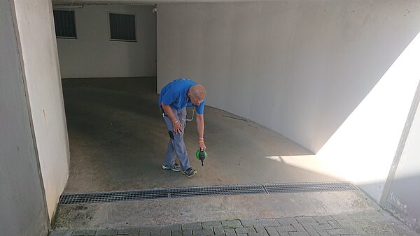 Das Bild zeigt einen Mitarbeiter der KABS bei der Tigermückenbekämpfung in einer Abflussrinne einer Einfahrt. 