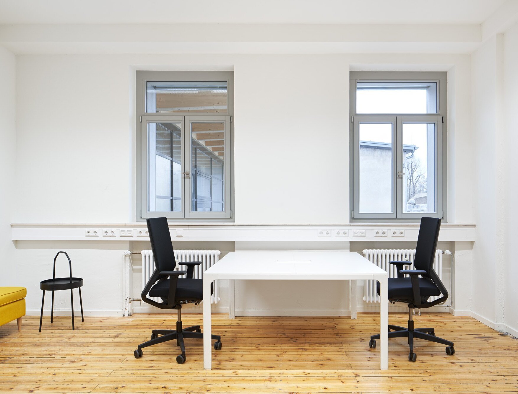 Das Bild zeigt ein möbliertes Büro mit Holzboden und hellgrauen Fenstern.