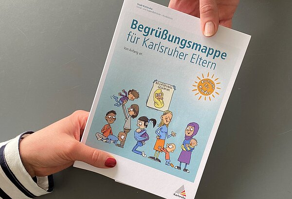 Eine Hand gibt eine Begrüßungsmappe an eine andere Hand weiter.