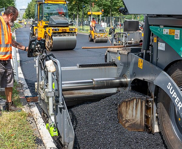 Bei der Baustelle an der Ludwig-Erhard-Allee wird zur Fahrbahnsanierung ein neuartiger Niedertemperaturasphalt auf der Fahrbahn aufgebracht.