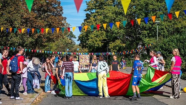 Mehrere Kinder halten ein buntes Schwungtuch im Rahmen der Aktion Karlsruhe spielt! 2026