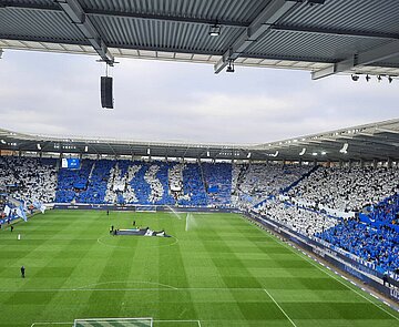 KSC-Spiel gegen Hertha BSC mit Fans, die blau und weiße Plakate hochhalten, die den Schriftzug KSC bilden.