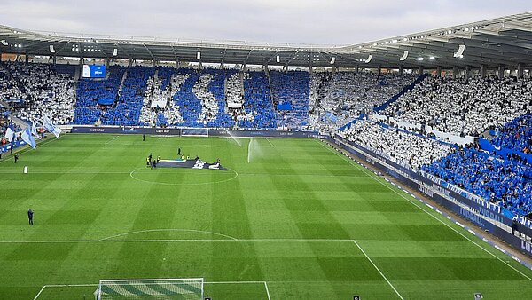 KSC-Spiel gegen Hertha BSC mit Fans, die blau und weiße Plakate hochhalten, die den Schriftzug KSC bilden.