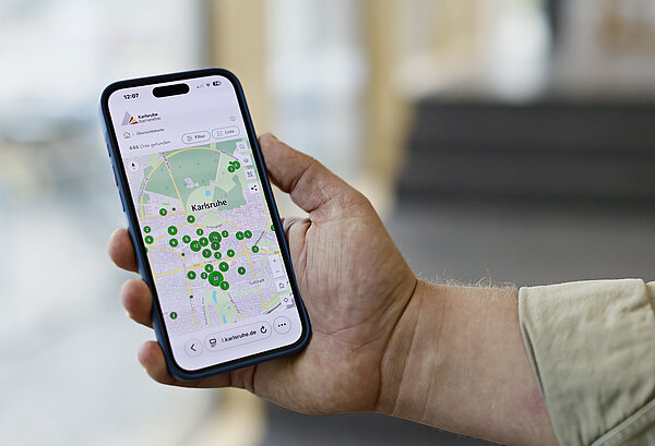 Hand hält Smartphone, das die Web-App Karlsruhe barrierefrei anzeigt.