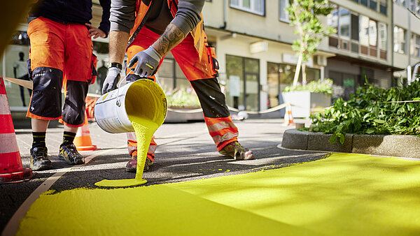 Personen schütten gelbe Farbe aus einem Farbeimer auf den Boden im Passgehof