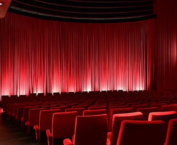 Sitzreihen im Kinosaal mit geschlossenem Vorhang vor der Leinwand.