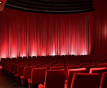 Sitzreihen im Kinosaal mit geschlossenem Vorhang vor der Leinwand.