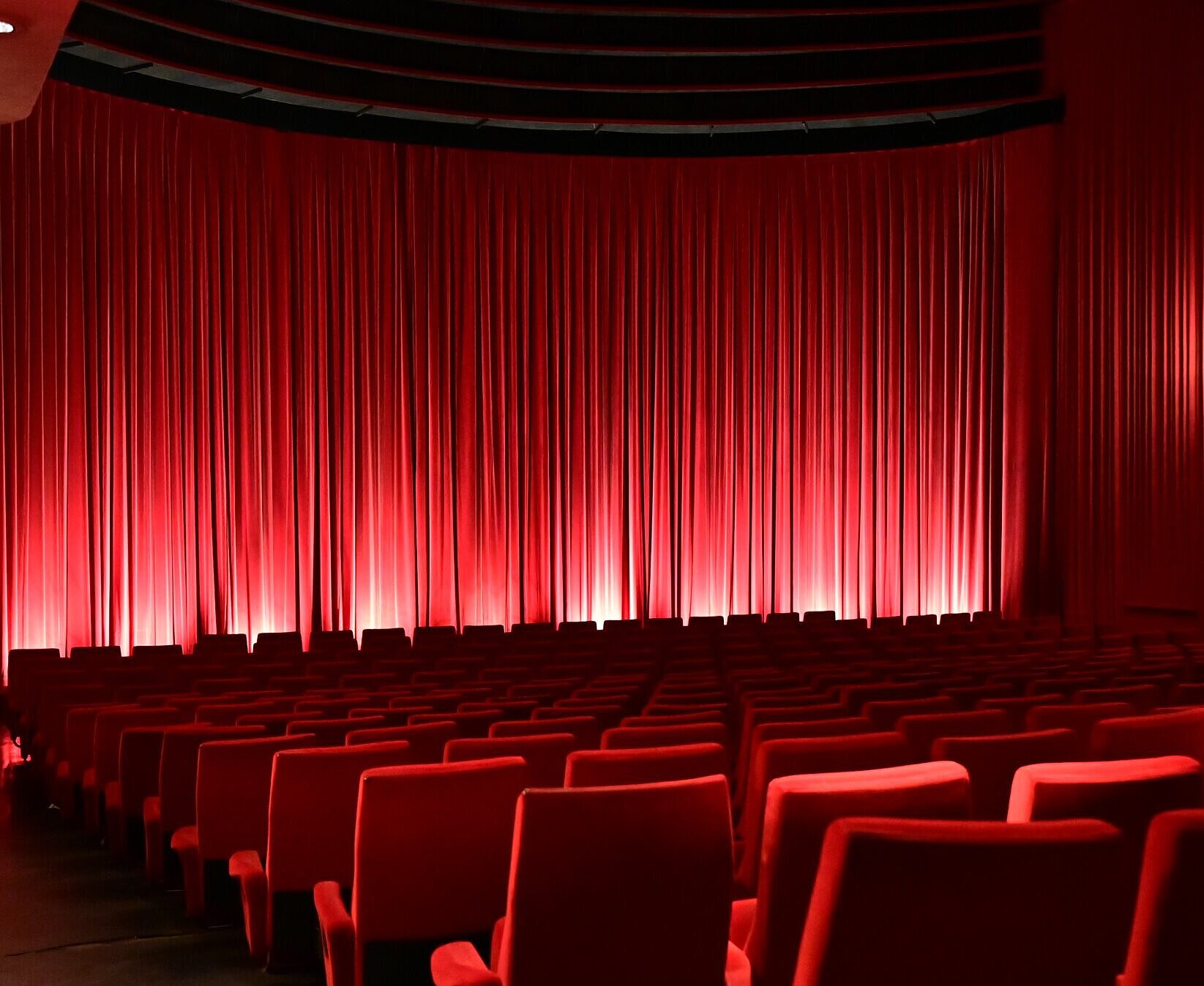 Sitzreihen im Kinosaal mit geschlossenem Vorhang vor der Leinwand.