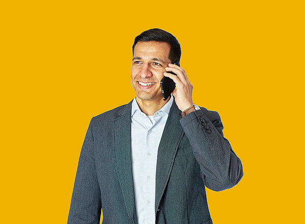 Mitarbeiter steht telefonierend vor gelbem Hintergrund