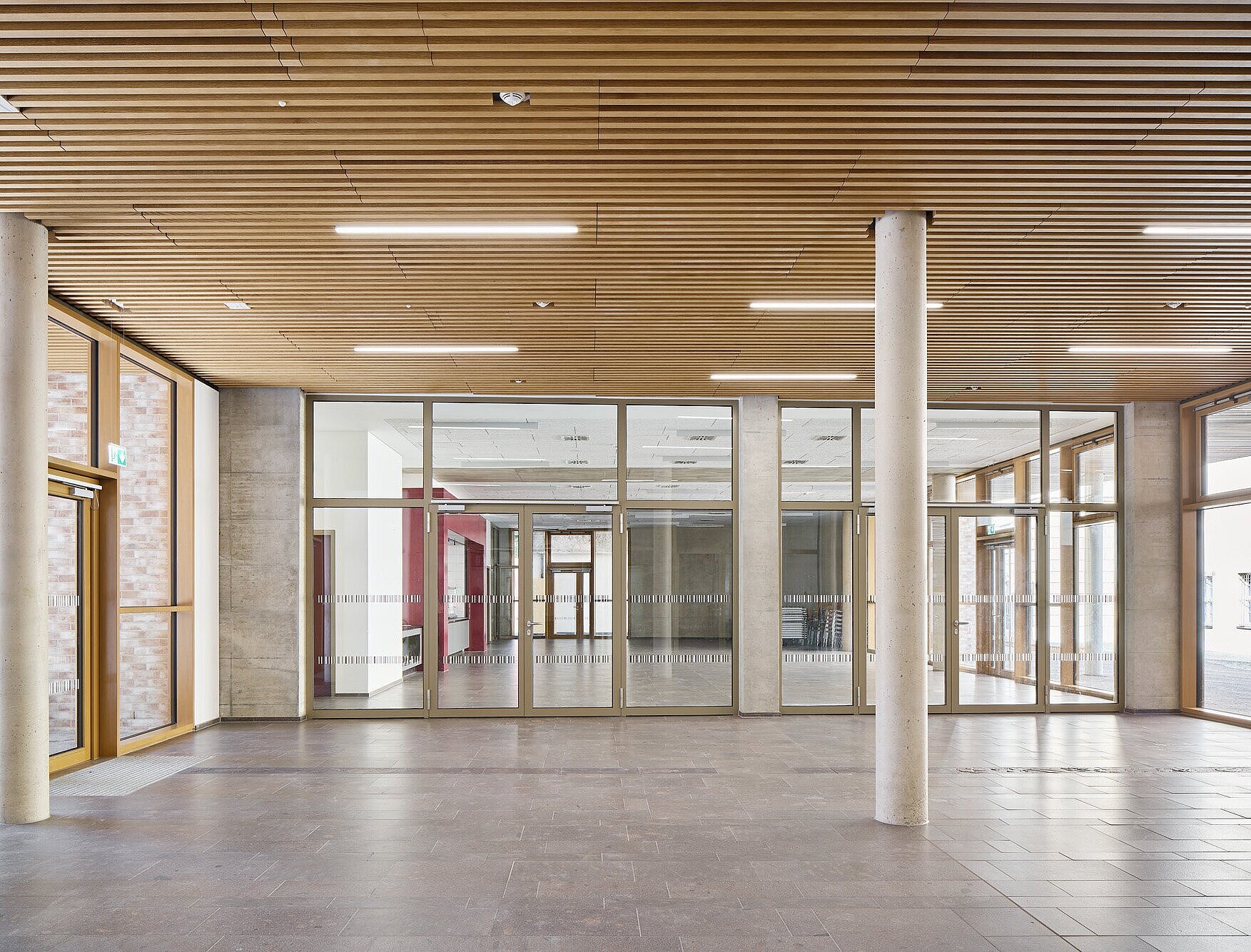 Zu sehen ist der helle und freundliche Innenbereich der Pausenfläche. Der Raum hat eine Decke mit Holzlamellen, große bodenhohe Fensterflächen und einen Porphyr-Steinboden.