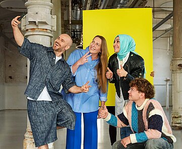 Eine Gruppe bestehend auf fünf Personen unterschiedlichen Alters und Geschlechts machen ein Selfie und blicken lachend in die Handykamera.