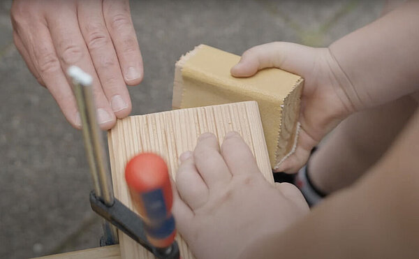 Filmstill: Eine Person schleift ein Brett.