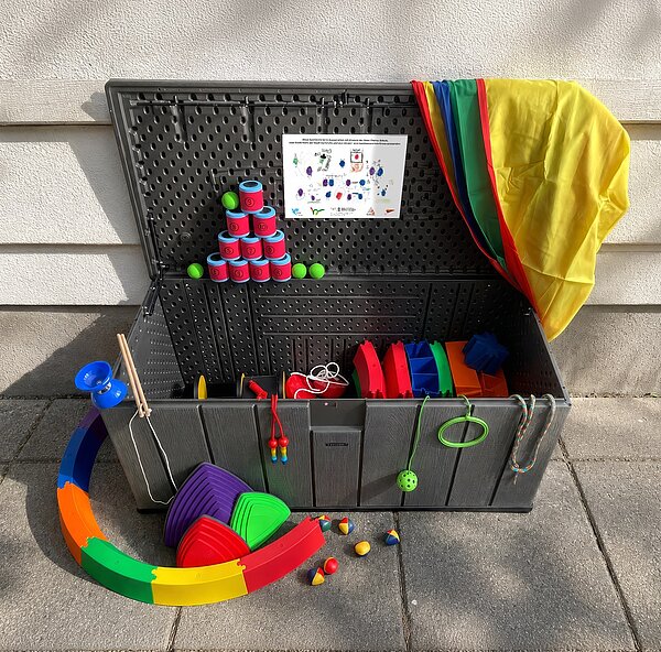 Geöffnete Kiste mit verschiedenen, bunten Spielsachen wie zum Beispiel: Diabolo, Dosenwerfen, Springseil, Jonglierbälle und so weiter