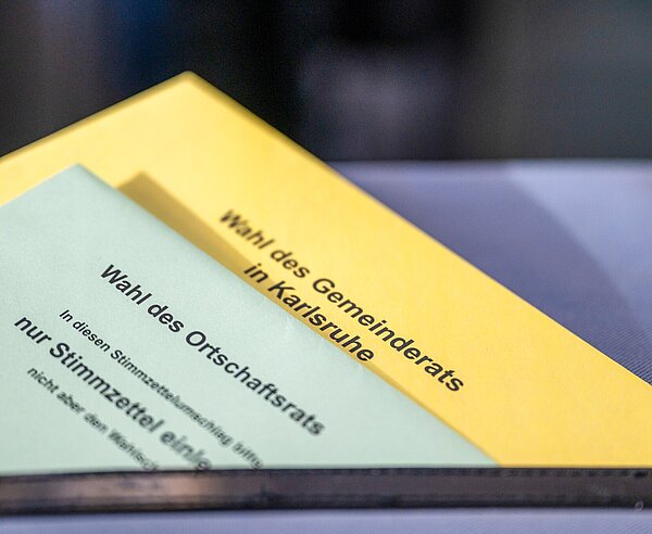 Nahaufnahme von Stimmzettelumschlägen für die Wahl des Gemeinderats und die Wahl des Ortschaftsrats halb im Schlitz einer Wahlurne.