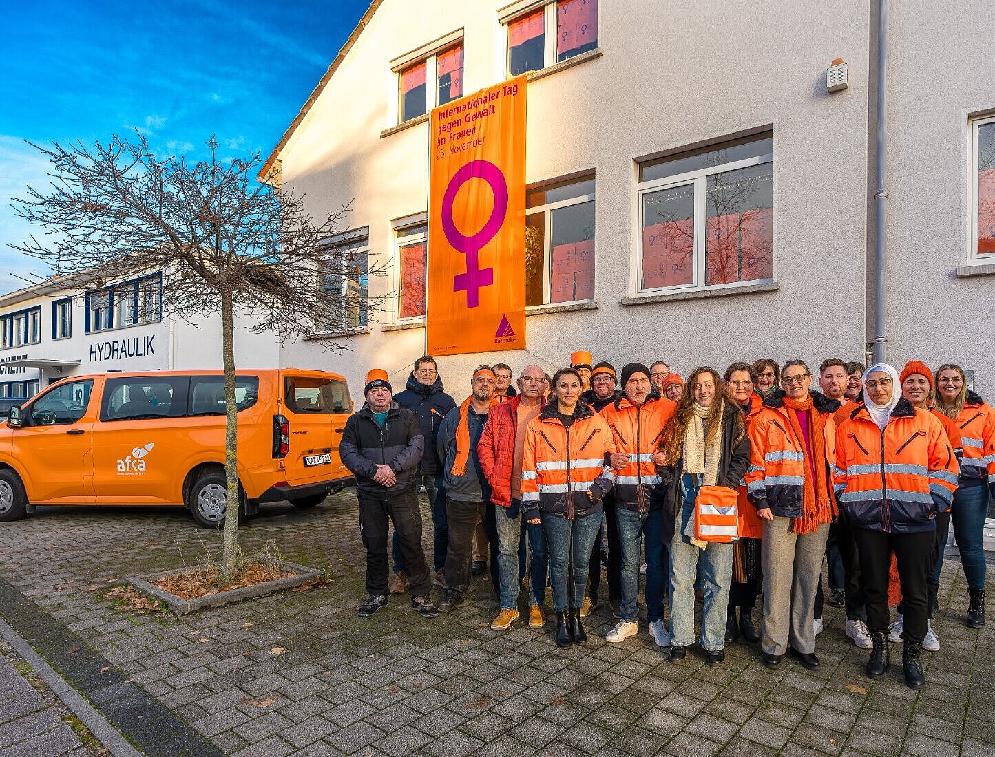 Im Vordergrund Mitarbeitende Arbeitsförderungsbetriebe, im Hintergrund eine Fahne zum Internationalen Tag gegen Gewalt am Gebäude