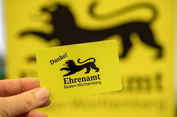 Hand hält gelbe Ehrenamtskarte Baden-Württemberg 