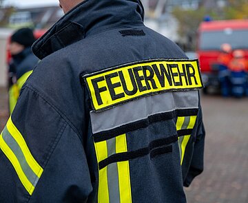 Rücken eines Feuerwehrmensch mit Feuerwehrjacke und Aufschrift "Feuerwehr"