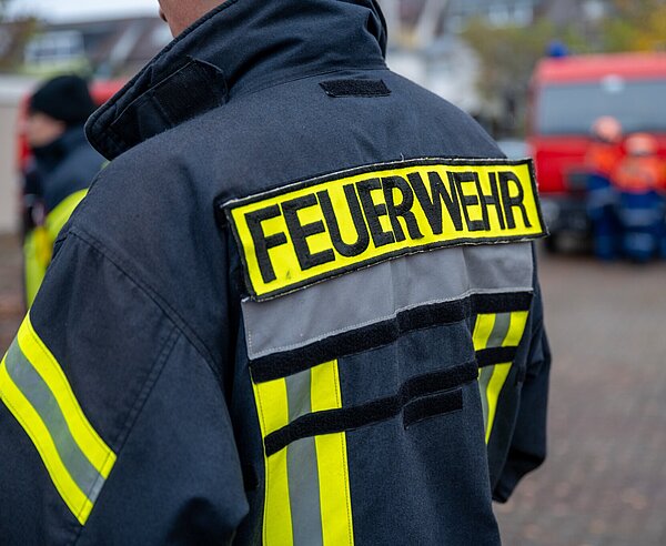 Rücken eines Feuerwehrmensch mit Feuerwehrjacke und Aufschrift "Feuerwehr"