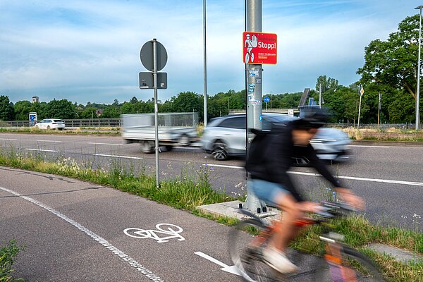Radfahrer auf dem Radweg mit Autoverkehr im Hintergrund und dem Hinweisschild auf die Gefahrenstelle durch Geisterradler
