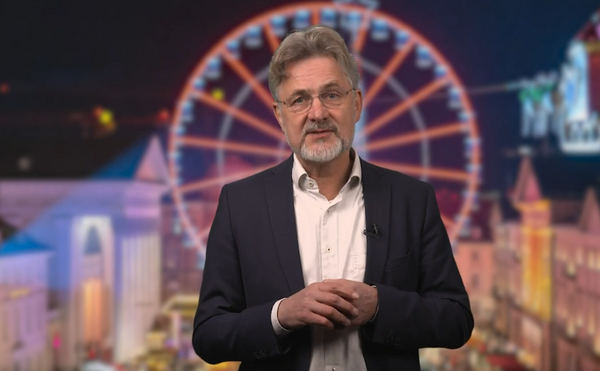 Das Bild zeigt Bürgermeister Dr. Frank Mentrup vor den Kulissen des Weihnachtsmarkts am Karlsruher Marktplatz,im Hintergrund ist ein Riesenrad zu sehen.