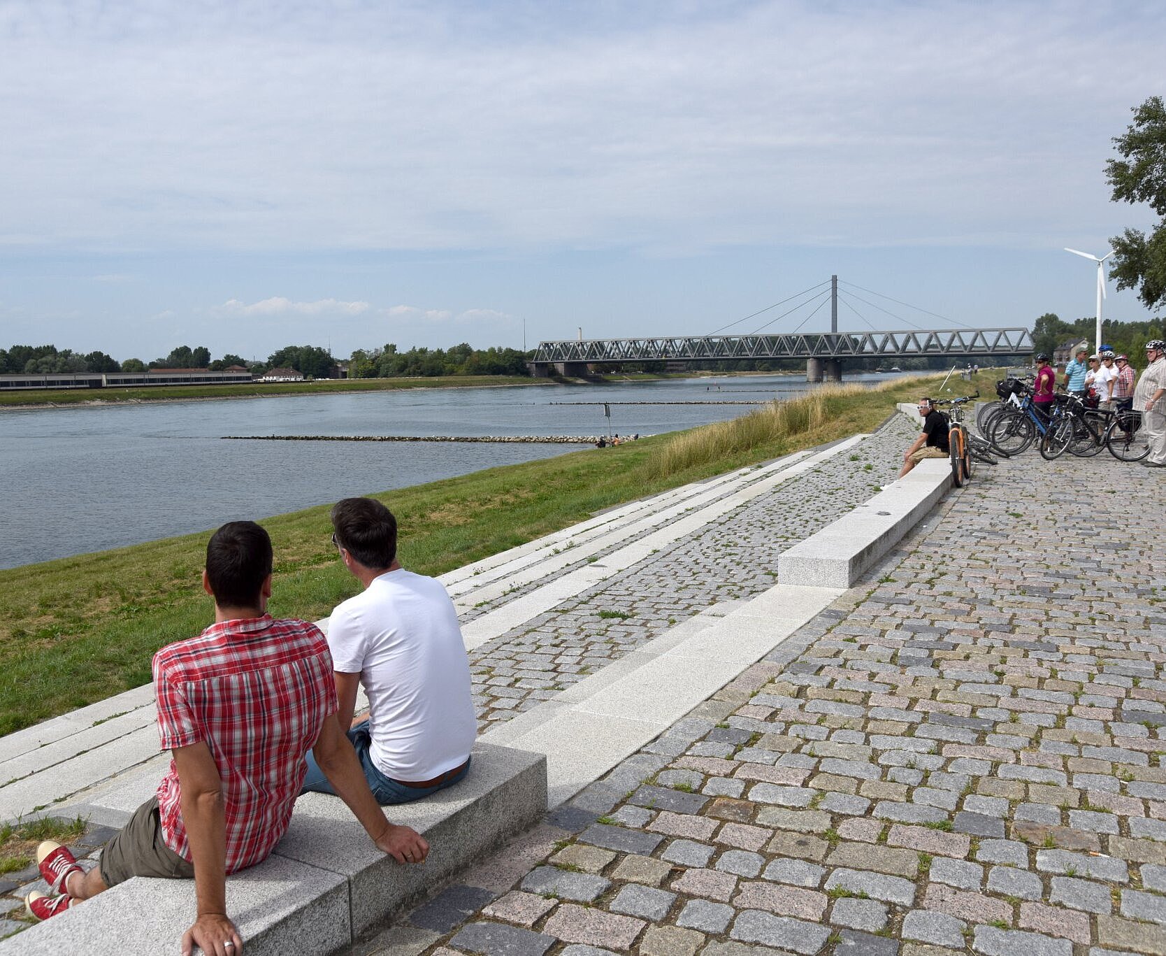 Zwei Männer sitzen auf einer Steinbank und gucken auf den Rhein.