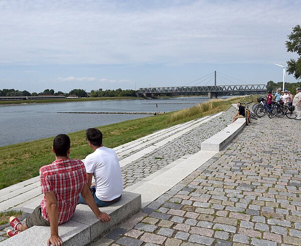 Zwei Männer sitzen auf einer Steinbank und gucken auf den Rhein.