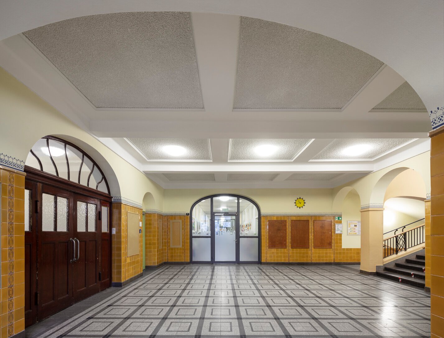 Blick in ein Foyer mit historischen Wandfliesen, Türen und saniertem Steinboden.