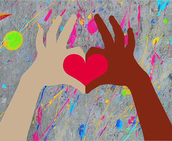 Eine dunkle und eine helle Hand formen mit Zeigefingern und Daumen ein rotes Herz. Hintergrund ist eine buntbekleckste Betonwand. Links oben ist der Kinderbüro Papierflieger zu sehen.