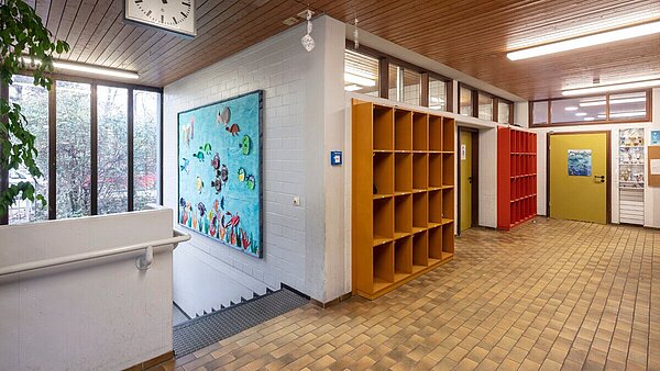 Zu sehen ist der Flurbereich vor der Sanierung mit alten Fliesen, Holzdecke und den abgenutzten Türblättern.