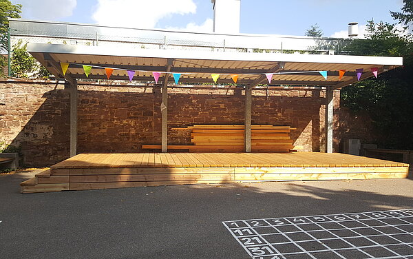 Das Bild zeigt ein Holzpodest im Schulhof der Grundschule Knielingen.