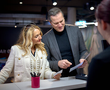 Hier ist ein Paar zu sehen, welches an der Hotelrezeption steht.