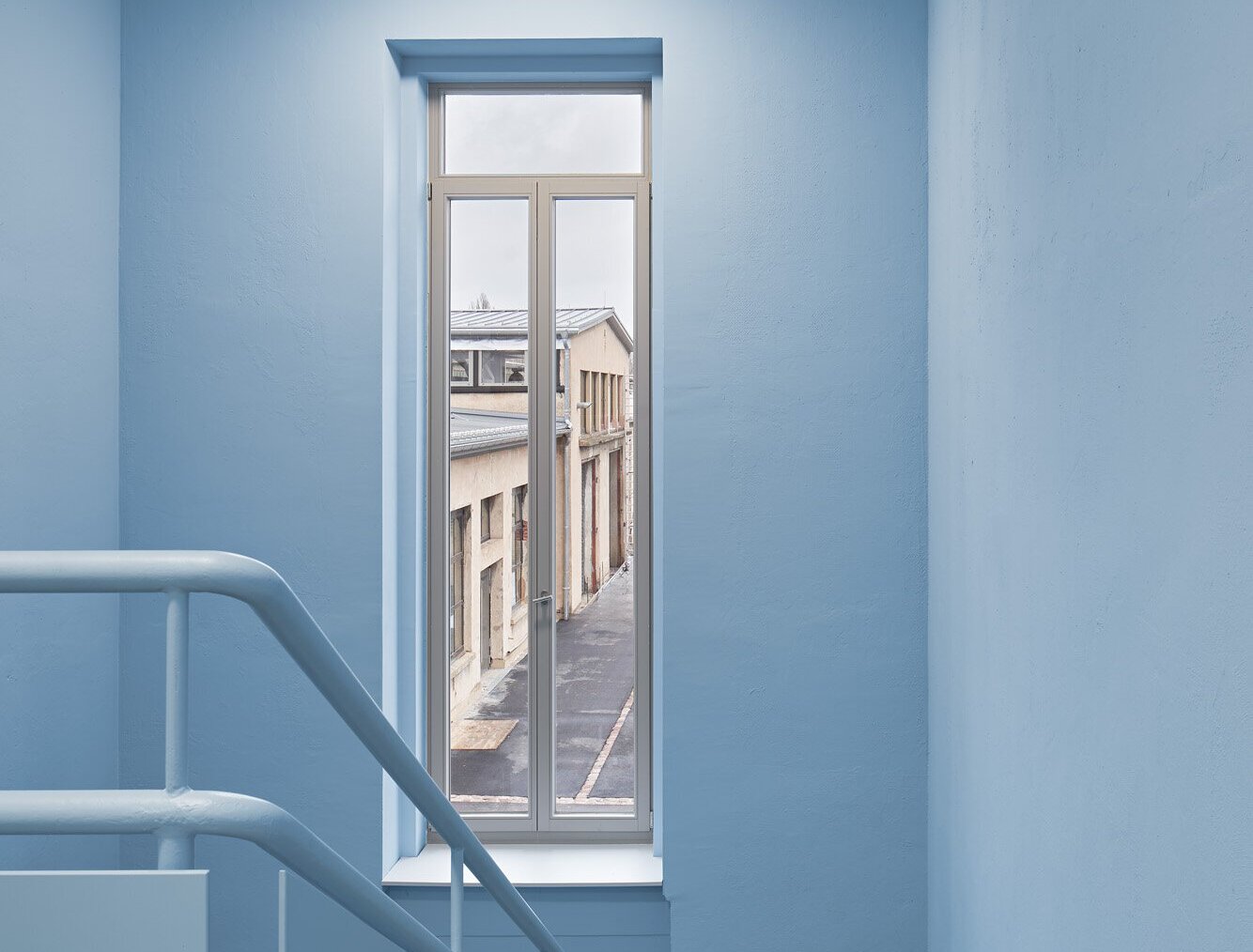 Das Bild zeigt das Treppenhaus des Verwaltungsgebäudes mit hellblauem Anstrich und grauen Fliesen.