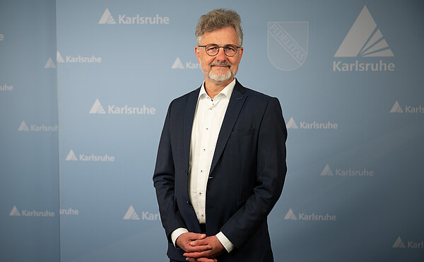 Oberbürgermeister Dr. Mentrup stehend vor blauer Wand auf der das Logo und das Wappen der Stadt abgebildet sind