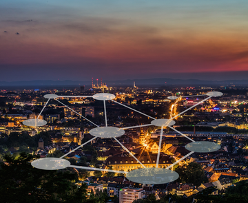 Stadt Karlsruhe von oben bei Nacht, darüber schwebend ein Netzwerk mit bunten Zylindern