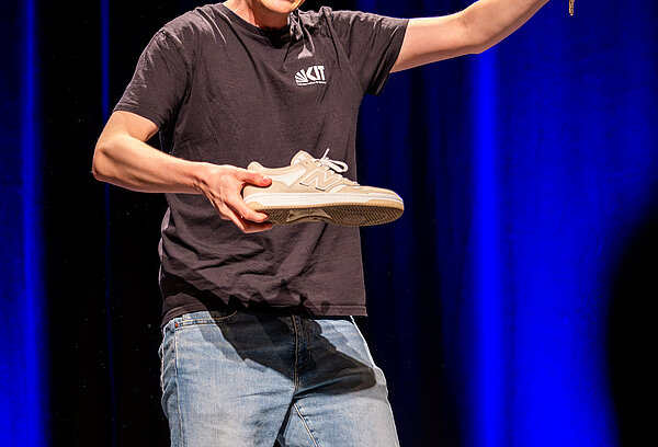 Der Gewinner erklärt sein Thema mit einem Schuh und einem Schlüssel in der Hand.