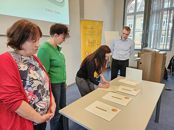 Meri Uhlig, Integrationsbeauftragte der Stadt Karlsruhe, unterzeichnet die Kooperationsvereinbarung im Beisein der Vertreterinnen und Vertreter der Partnerorganisationen von AniKA während des Bündnistreffens .