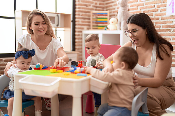 Lehrer und Vorschulkinder spielen mit Bauklötzen, die auf einem Tisch im Kindergarten sitzen.