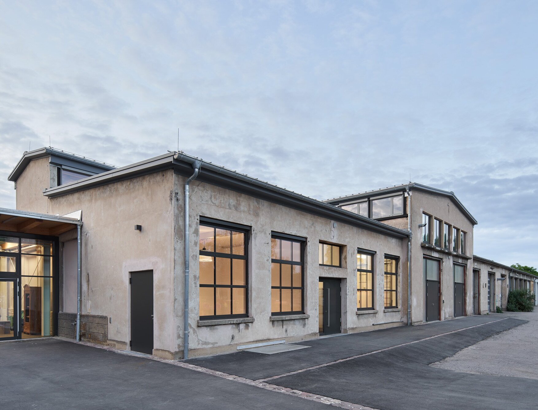 Zu sehen ist die beleuchtete Südansicht der ehemaligen Reparaturhalle in der Dämmerung.