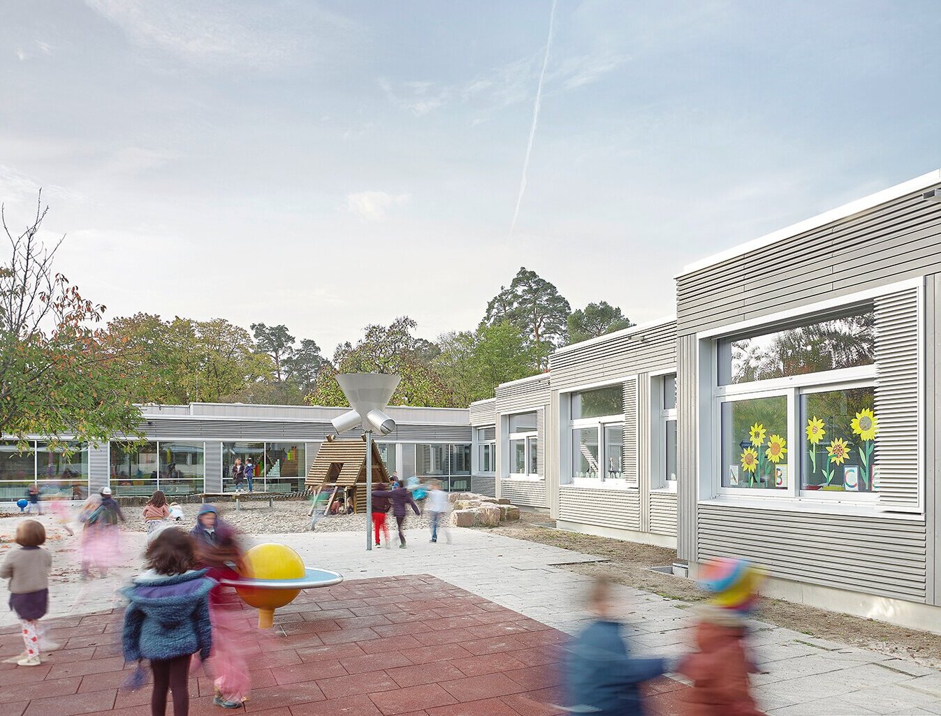 Zu sehen sind spielende Kinder im Spielgarten und die sanierte Fassade des Gebäudes im Hintergrund.