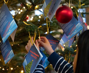 Eine Schülerin des Horts der Grundschule am Wasserturm hängt im Rathausfoyer einen Wunschzettel an einen Zweig des Weihnachtsbaumes