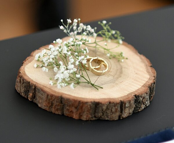 Zwei goldene Ringe auf einer Holzscheibe mit Blümchen.