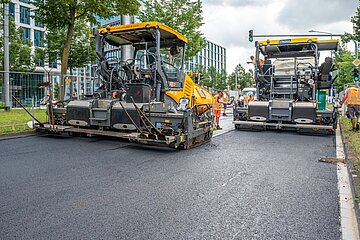 Bei der Baustelle an der Ludwig-Erhard-Allee wird zur Fahrbahnsanierung ein neuartiger Niedertemperaturasphalt auf der Fahrbahn aufgebracht.