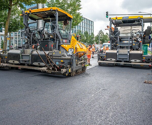 Bei der Baustelle an der Ludwig-Erhard-Allee wird zur Fahrbahnsanierung ein neuartiger Niedertemperaturasphalt auf der Fahrbahn aufgebracht.