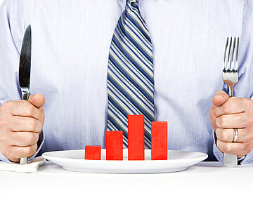 Ein Mann sitzt mit Messer und Gabel vor einem Säulendiagramm auf dem Teller
