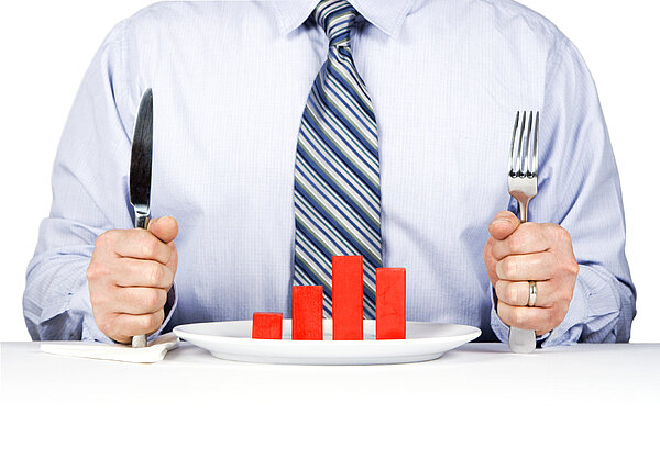 Ein Mann sitzt mit Messer und Gabel vor einem Säulendiagramm auf dem Teller