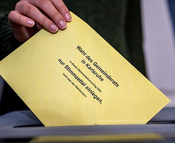 Person wirft Stimmzettelumschlag für die Wahl des Gemeinderats in die Urne